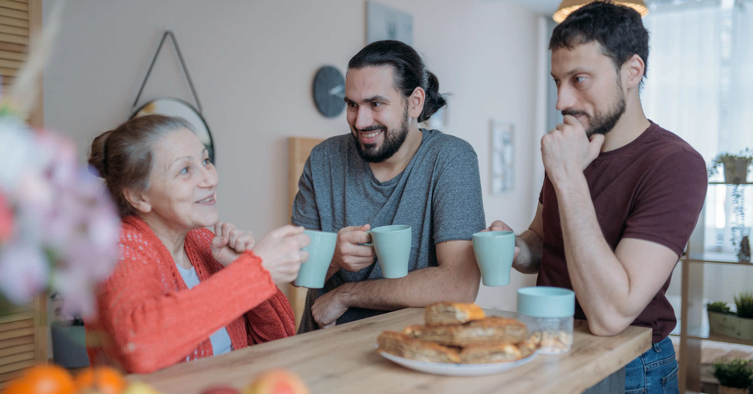 adult brothers chatting with mother in kitchen over coffee